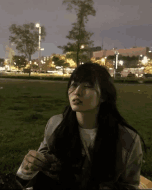 a woman is sitting in the grass with her eyes closed at night