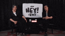 two people are sitting in front of a sign that says hey