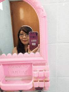 a woman is taking a picture of herself in a pink mirror that says manos limpias