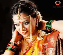 a woman in a traditional indian wedding dress is wearing a nose ring , necklace , and bangles .