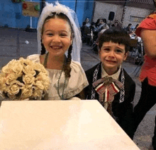 a little girl dressed as a bride and a little boy dressed as a groom are sitting next to each other .