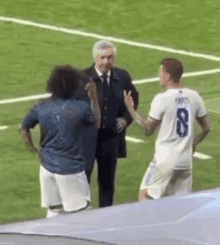 a man in a suit and tie is standing on a soccer field talking to two soccer players .