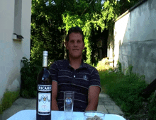 a man sitting at a table with a bottle of ricard on it