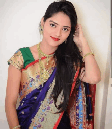 a woman in a blue saree and gold jewelry is standing in front of a wall .