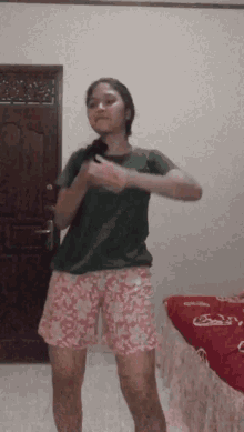 a woman in a green shirt and pink shorts is dancing in front of a door