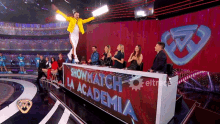 a man in a yellow jacket stands on a stage in front of a showmatch la academia sign