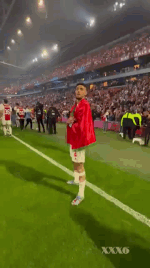 a man in a red and green shirt is walking on a soccer field with a crowd in the background .