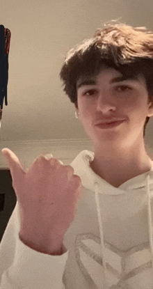 a young man in a white hoodie is giving a thumbs up sign