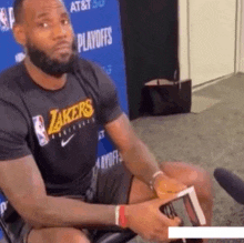 a man wearing a lakers t-shirt sits in front of a microphone