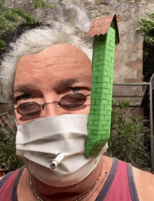 a man wearing a mask smoking a cigarette with a green house on his head