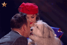 a woman in a red hat is kissing a man and a white dog