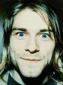 a close up of a man 's face with long hair and blue eyes