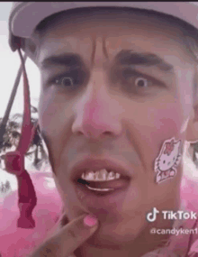 a man with a hello kitty sticker on his face is wearing a pink helmet .