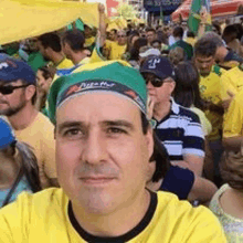 a man in a yellow shirt and green hat is taking a selfie in front of a crowd .