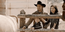 a man in a cowboy hat is standing next to a woman and a boy behind a fence .