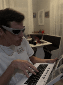 a man wearing sunglasses is typing on a laptop with a sticker on his shirt that says " i love you "