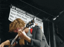 a man playing a guitar in front of a sign that says no moshing crowd surfing