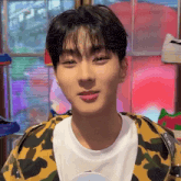 a young man wearing a camouflage jacket and a white t-shirt is smiling .