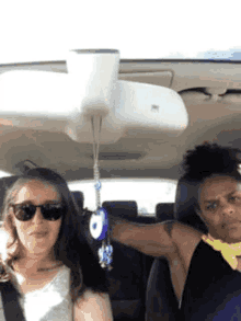 two women are sitting in a car with a rear view mirror hanging from the roof .