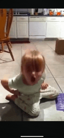 a little girl sitting on the floor with her mouth open