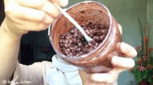 a person is holding a jar of chocolate covered rice with a spoon in it .