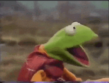 kermit the frog is wearing a red cape and looking at the camera with his mouth wide open .