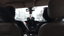 two people are sitting in a car with a rear view mirror hanging from the ceiling