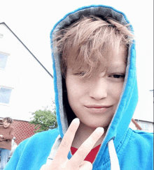 a boy wearing a blue hoodie is giving a peace sign