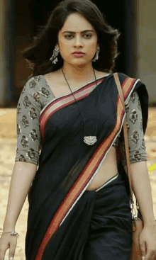 a woman in a black saree and a gray blouse is walking down a street .