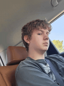 a young man with curly hair sits in a car