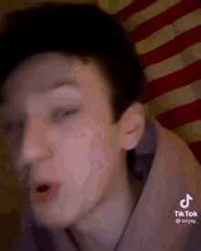 a young man is making a funny face in front of a red and white american flag .