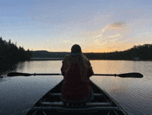 a woman sits in a canoe with oars in the water at sunset