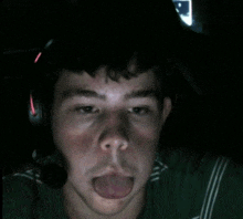 a man wearing a headset sticks his tongue out in the dark