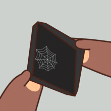 a person is holding a black square with a spider web drawing on it