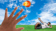 a man is laying on the grass while a hand reaches for a fireball