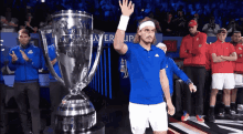 a man in a blue shirt stands in front of a trophy that says ' laver cup ' on it