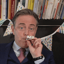 a man wearing a party hat holds a piece of cake in his mouth in front of a shelf of books including one called snow