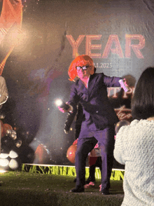 a man in a suit and orange wig is dancing in front of a sign that says year