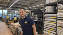 a man in a blue shirt is standing in a store next to a shelf filled with rolls of fabric .