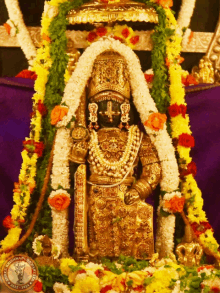 a statue of a deity is surrounded by flowers and garlands and has the year 2002 on the bottom right