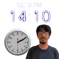 a man with glasses stands next to a clock that says 2:10 pm