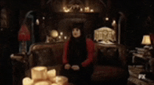 a woman in a red sweater is sitting on a couch in a dark room with candles .