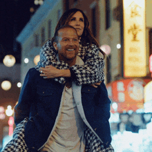 a man is carrying a woman on his shoulders in front of a sign that says ' hong kong '