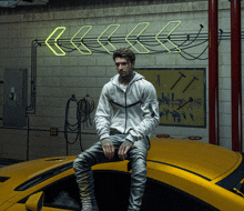 a man is sitting on the hood of a yellow sports car