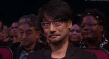 a man wearing glasses sits in a crowd at a game award show