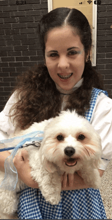 a woman is holding a small white dog in her arms and the time is 8:39