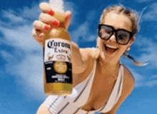 a woman in a bathing suit is holding a bottle of corona beer .