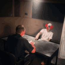 a man in a clown mask is sitting at a table with a police officer