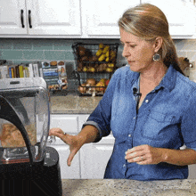 a woman in a denim shirt is using a blender in a kitchen with a plant based logo on the counter