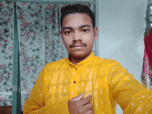 a man in a yellow shirt takes a selfie in front of a floral curtain